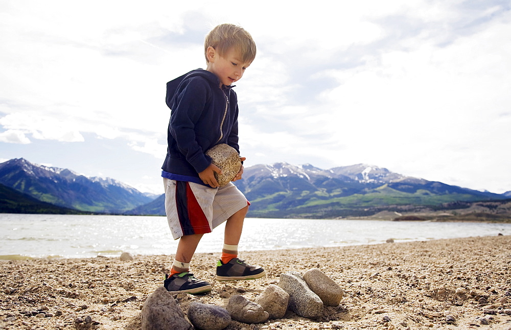 Boy (2-3) carrying rock on beach, Colorado, USA