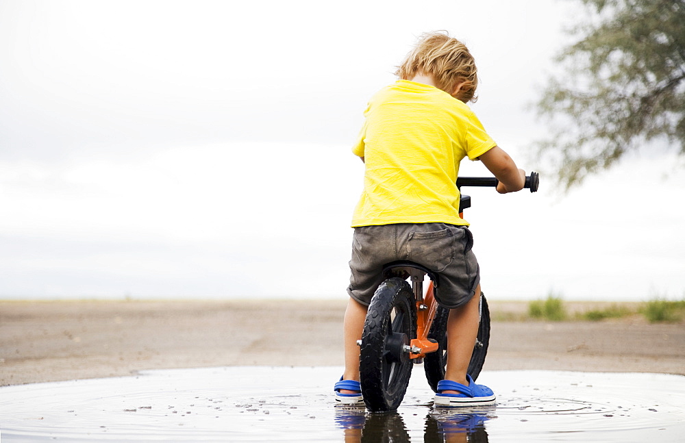 Toddler boy (2-3) riding bicycle in puddle, Colorado, USA