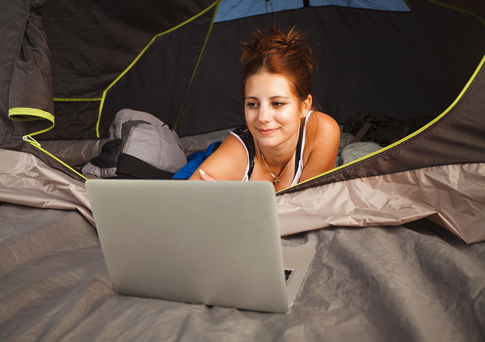 Hiker in tent using laptop, Switzerland, Leysin