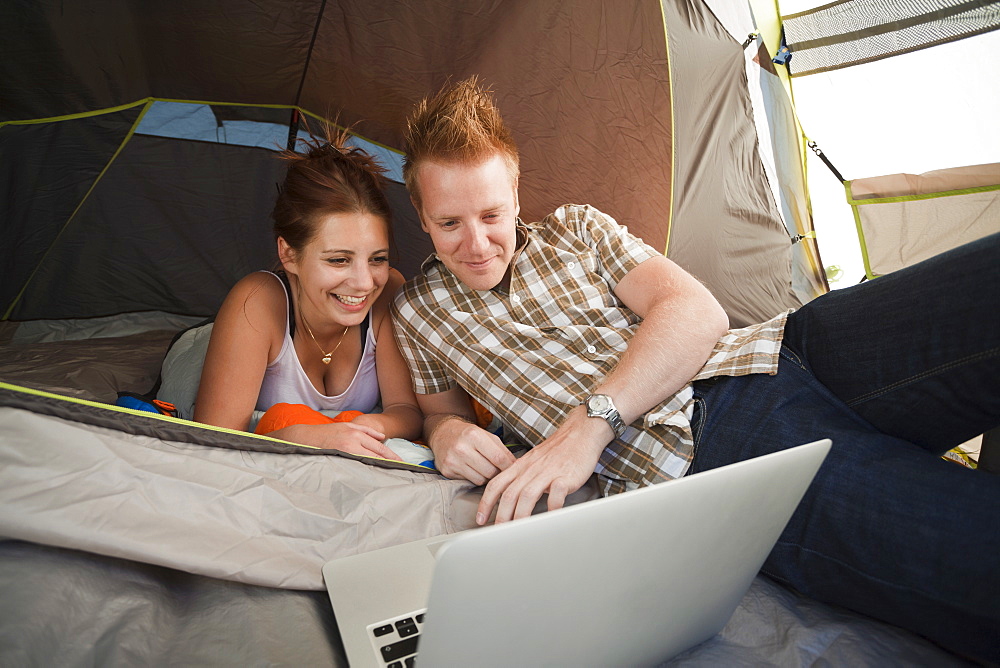 Hikers in tent using laptop, Switzerland, Leysin