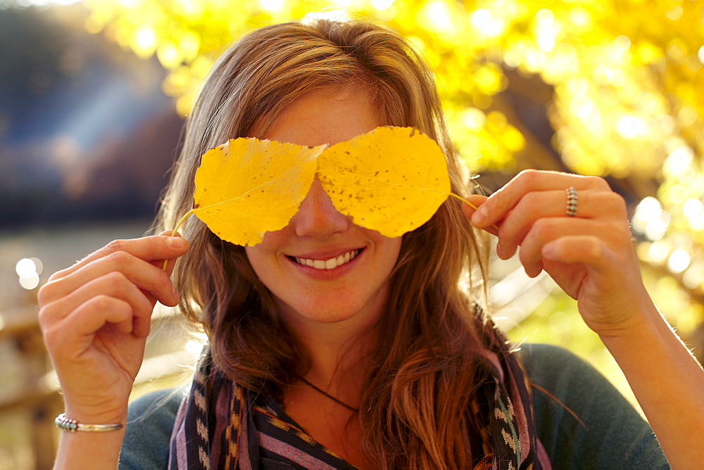 Woman covering eyes with autumn leaves