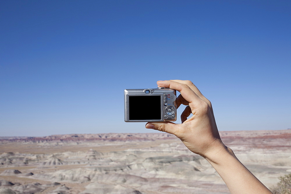 Hand of woman holding camera up against blue sky