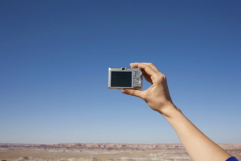 Hand of woman holding camera up against blue sky