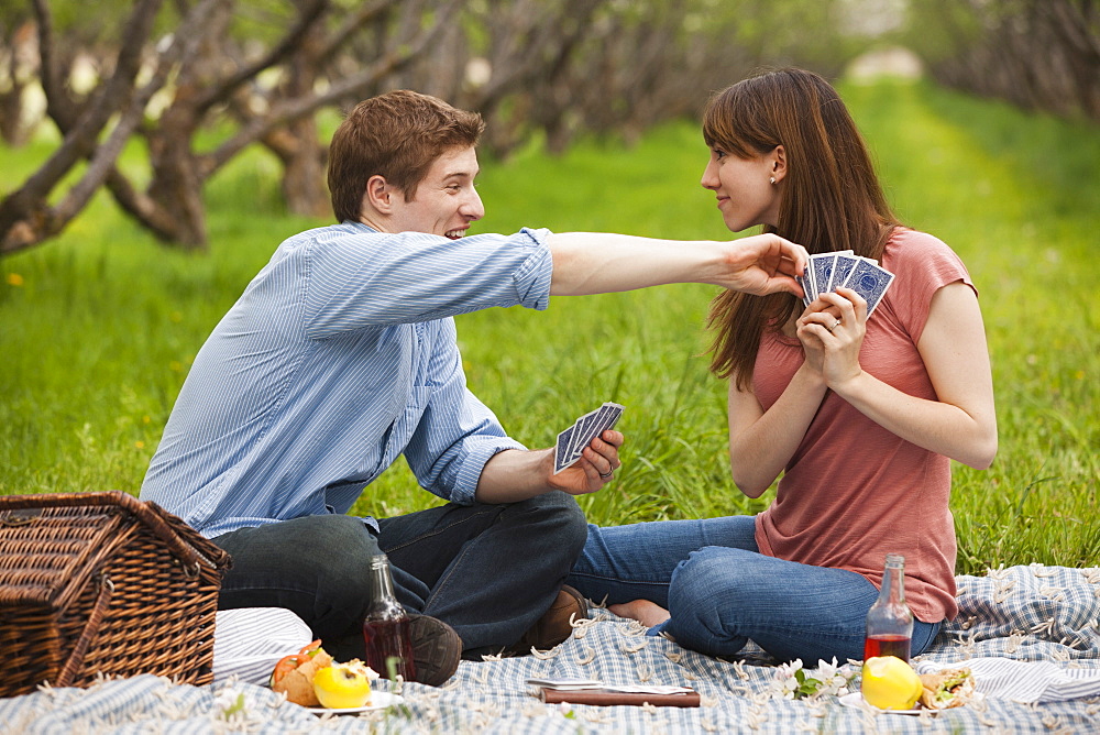 USA, Utah, Provo, Young couple playing cards during picnic in orchard