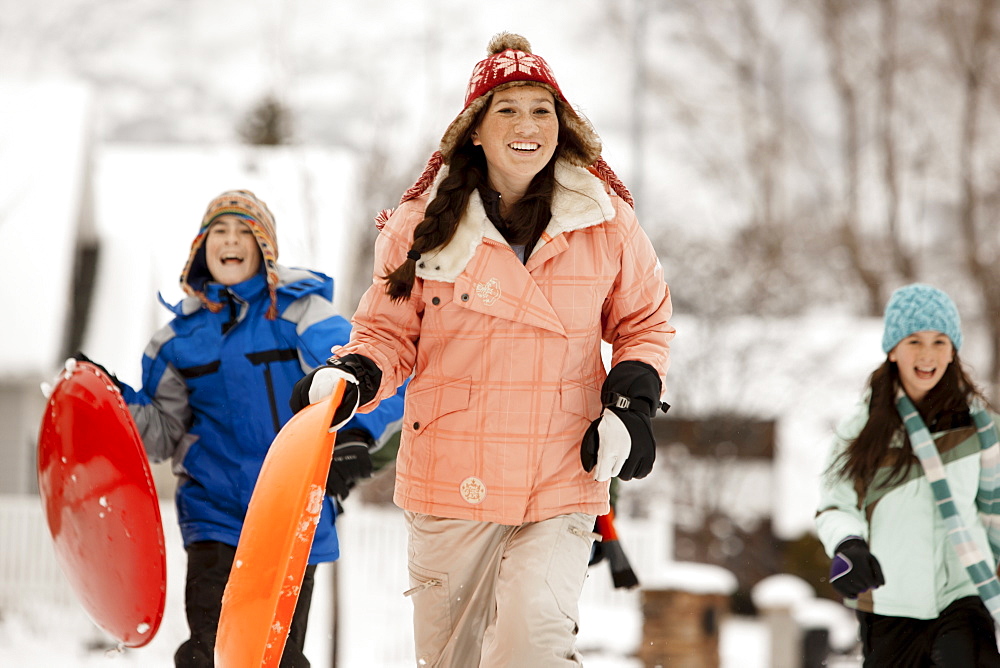 USA, Utah, Provo, Teenage (16-17) girl running with sledge, boys and girls (10-11, 12-13) in background