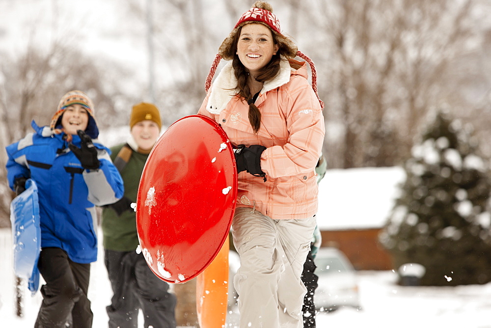 USA, Utah, Provo, Teenage (16-17) girl running with sledge, boys and girls (10-11, 12-13) in background