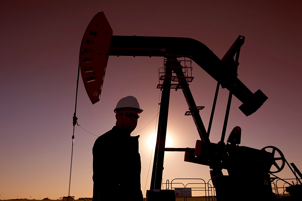 Silhouette of oil worker by pump jack on rig