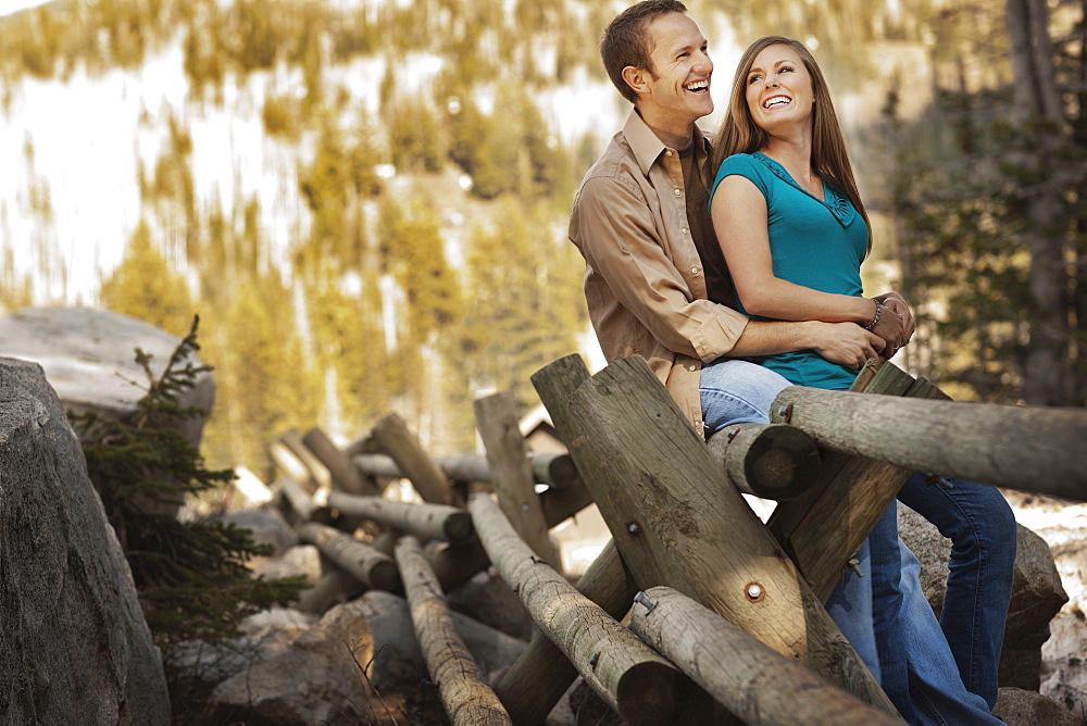 Laughing couple sitting on log fence