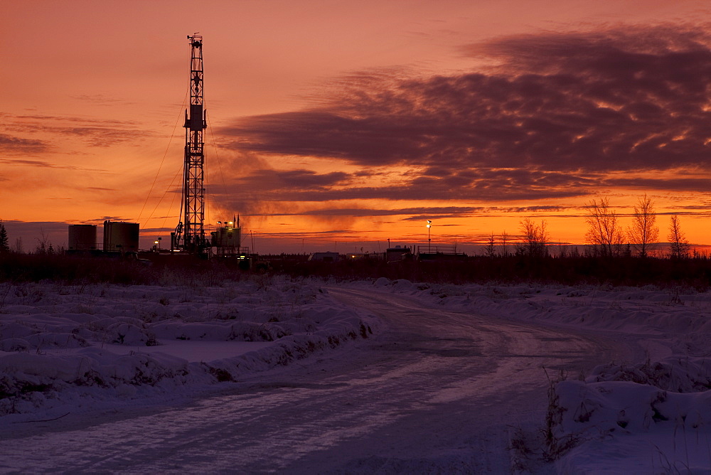 Snowy road at dusk with oil drilling rig in background