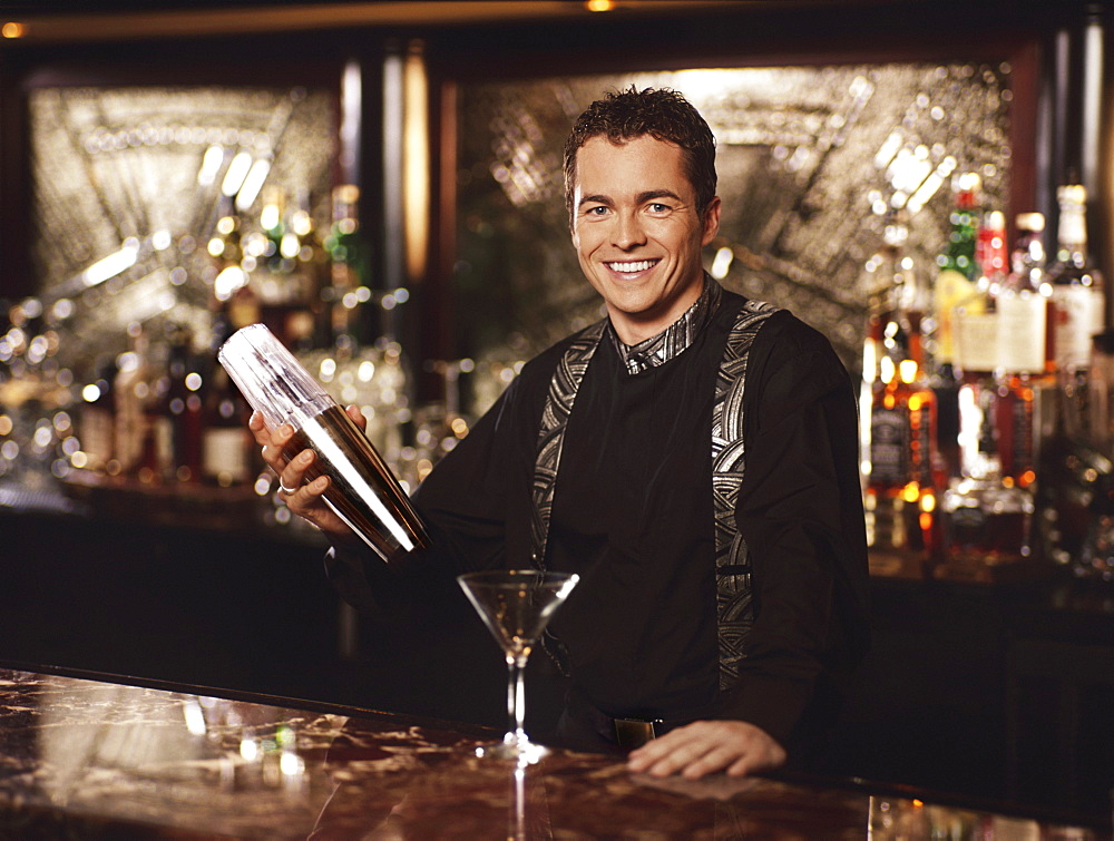 Young man standing behind bar shaking cocktail shaker, portrait