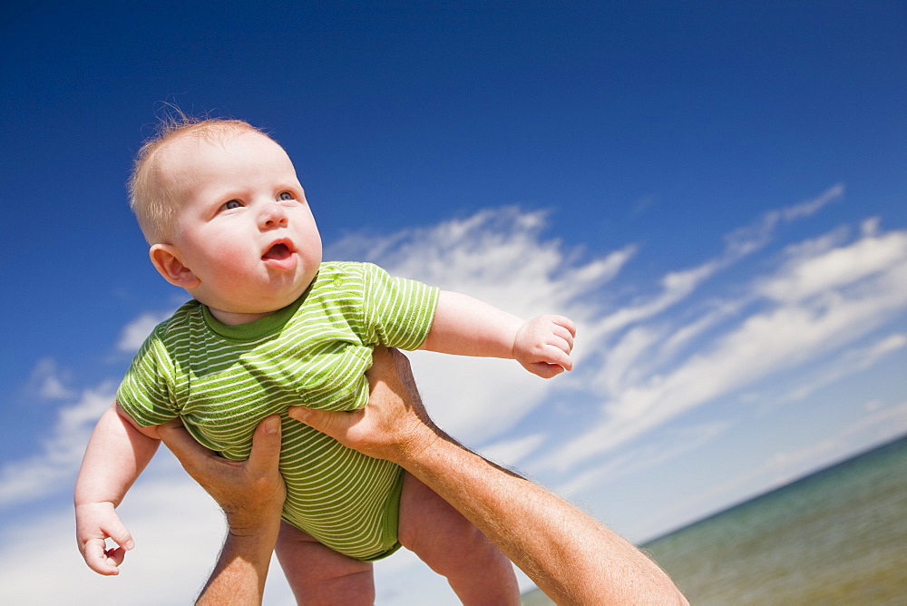 Senior man lifting baby in air, Beaver Island, Michigan, USA