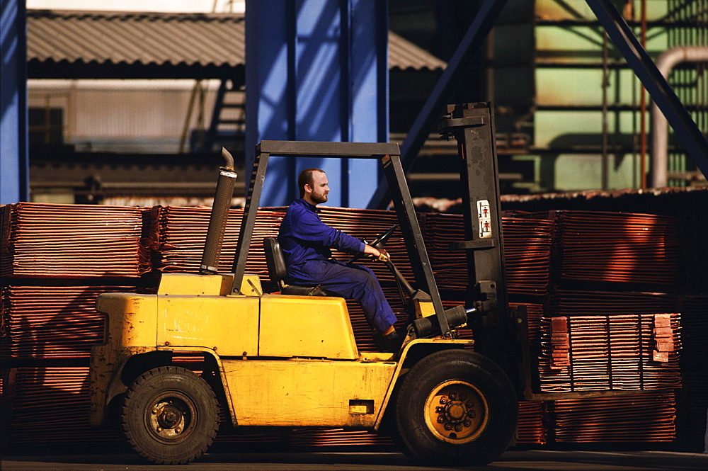 Worker lifting pallets of copper pipes on forklift