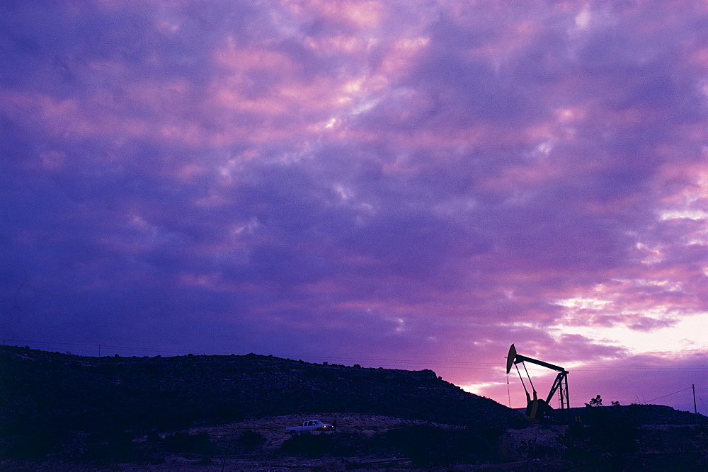 Oil rig in distance under sunset sky