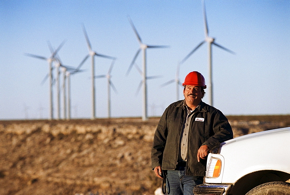 Worker leaning against truck with wind turbines in background