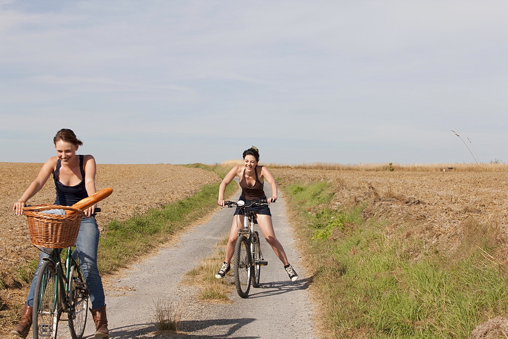 France, Picardie, Albert, Young women cycling on country road, France, Picardie, Albert
