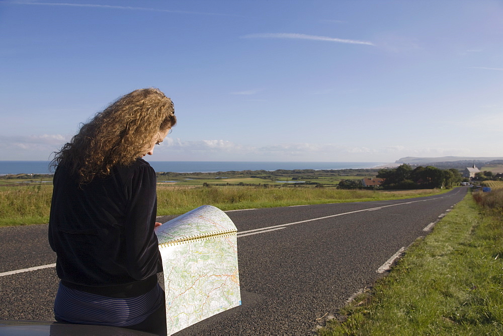 France, Pas-de-Calais, Escalles, Young woman reading map on roadside, France, Pas-de-Calais, Escalles