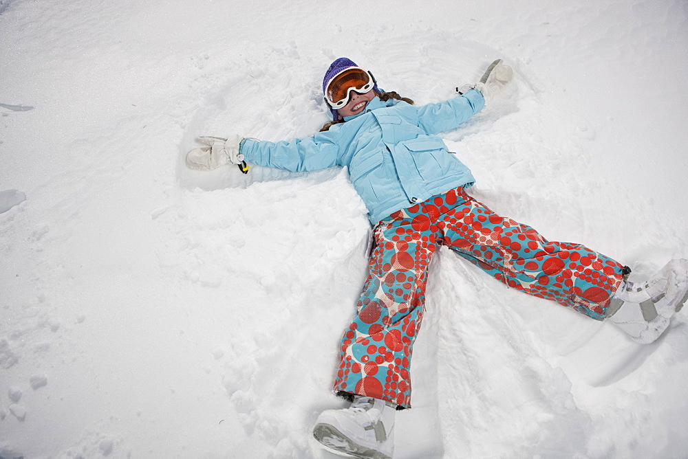 Girl (10-11) in ski gear doing snow angel