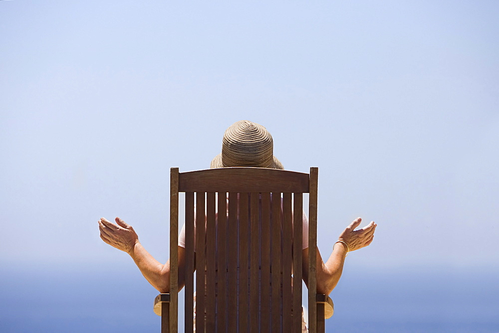 Spain, Costa Blanca, Rear view of woman sitting on wooden chair, facing sea