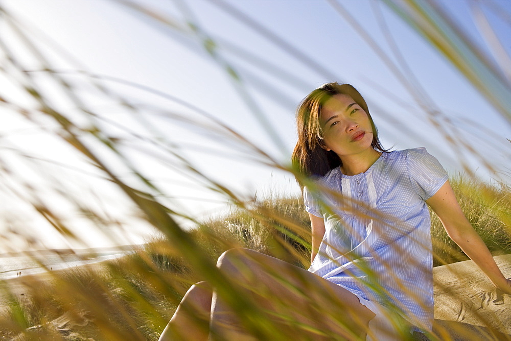 USA, California, Point Reyes, Young woman sitting in grass on sand dune