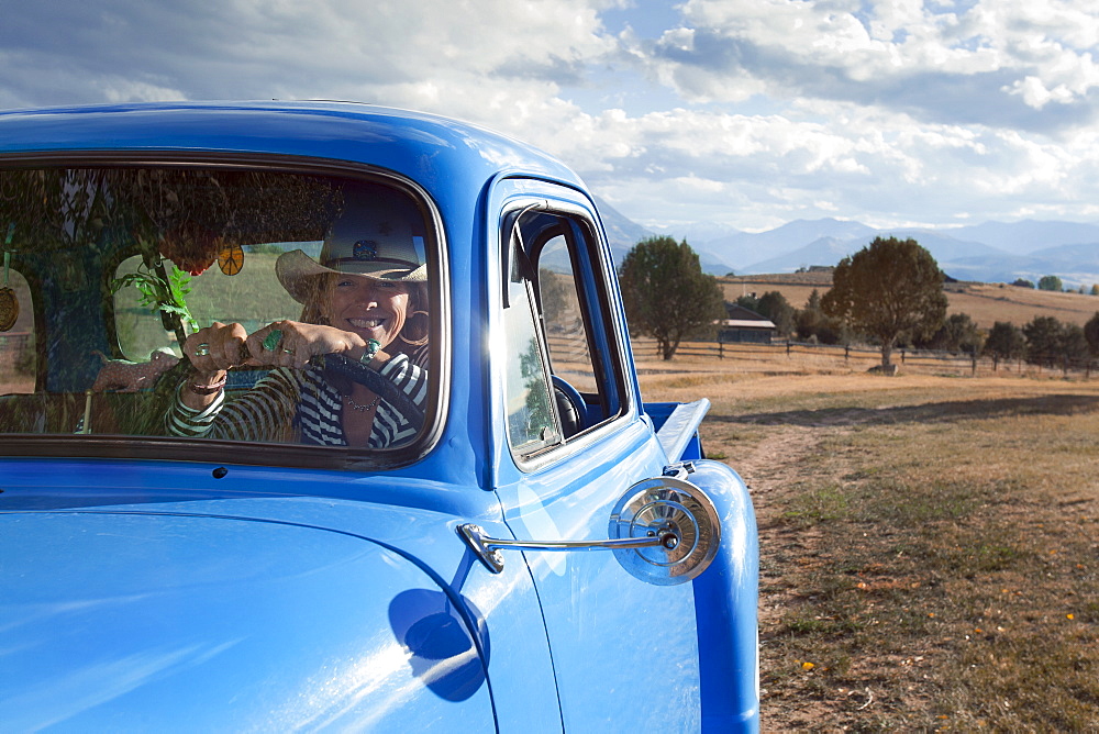 USA, Colorado, Carbondale, Cowgirl driving old fashioned pickup truck in field