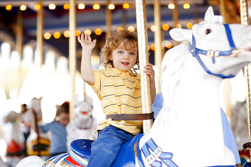 USA, California, Los Angeles, Boy (4-5) sitting on carousel's horse and waving