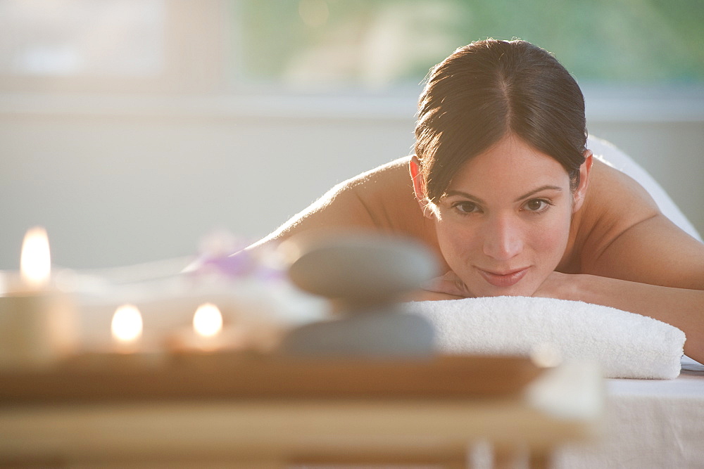 Mid-adult woman lying on massage table with candles and rocks in foreground