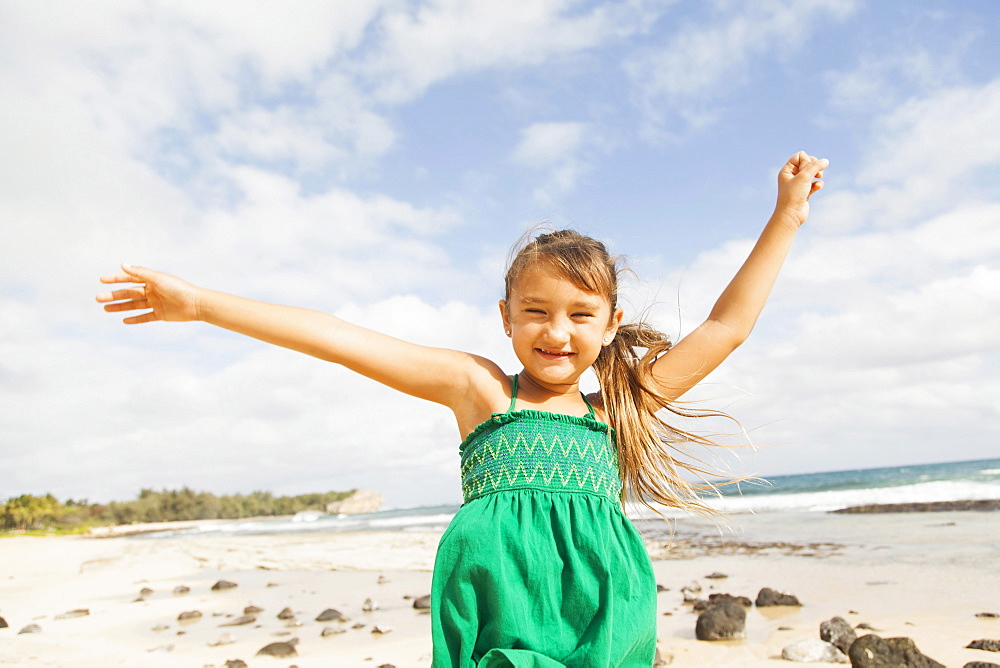 Portrait of girl (6-7) standing on beach with arms raised, Kauai, Hawaii