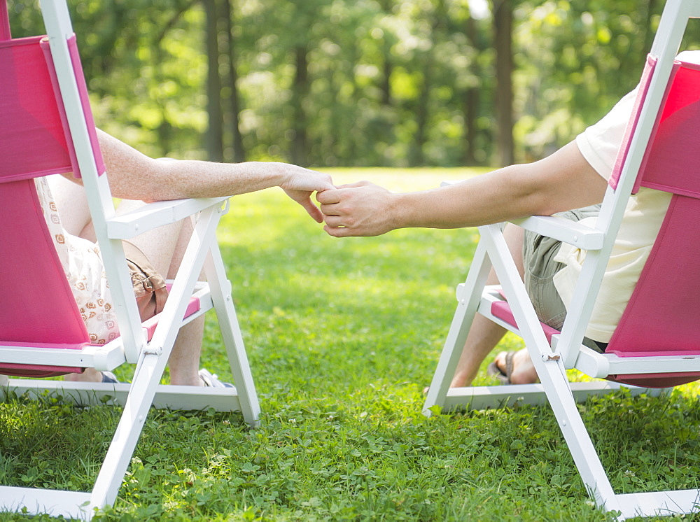 Couple sitting on deck chairs and holding hands, USA, New Jersey, Mendham