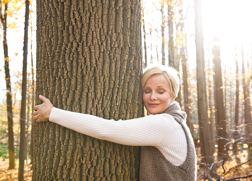 USA, New Jersey, Smiling woman hugging tree in Autumn forest