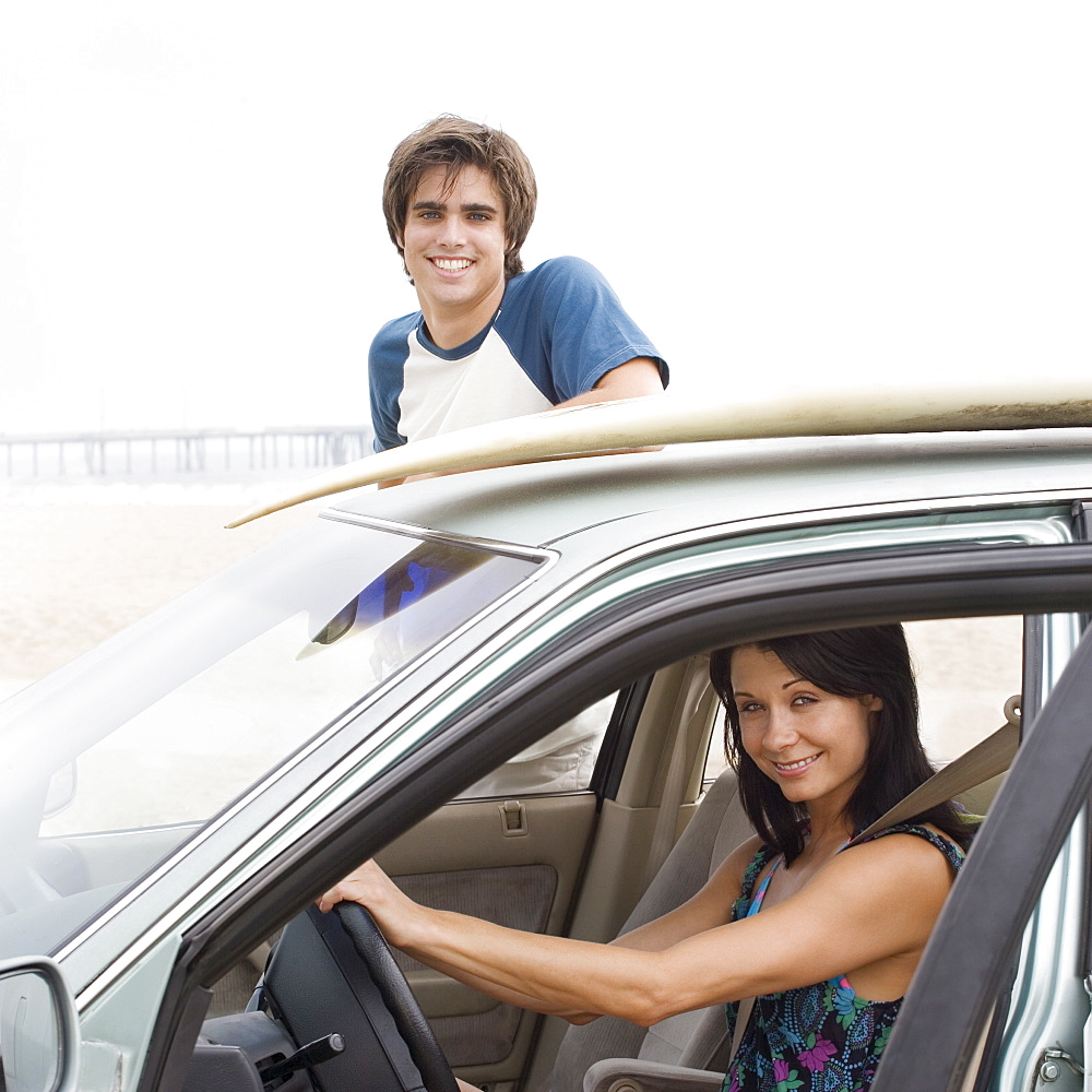 Couple and car with surfboard on top at beach