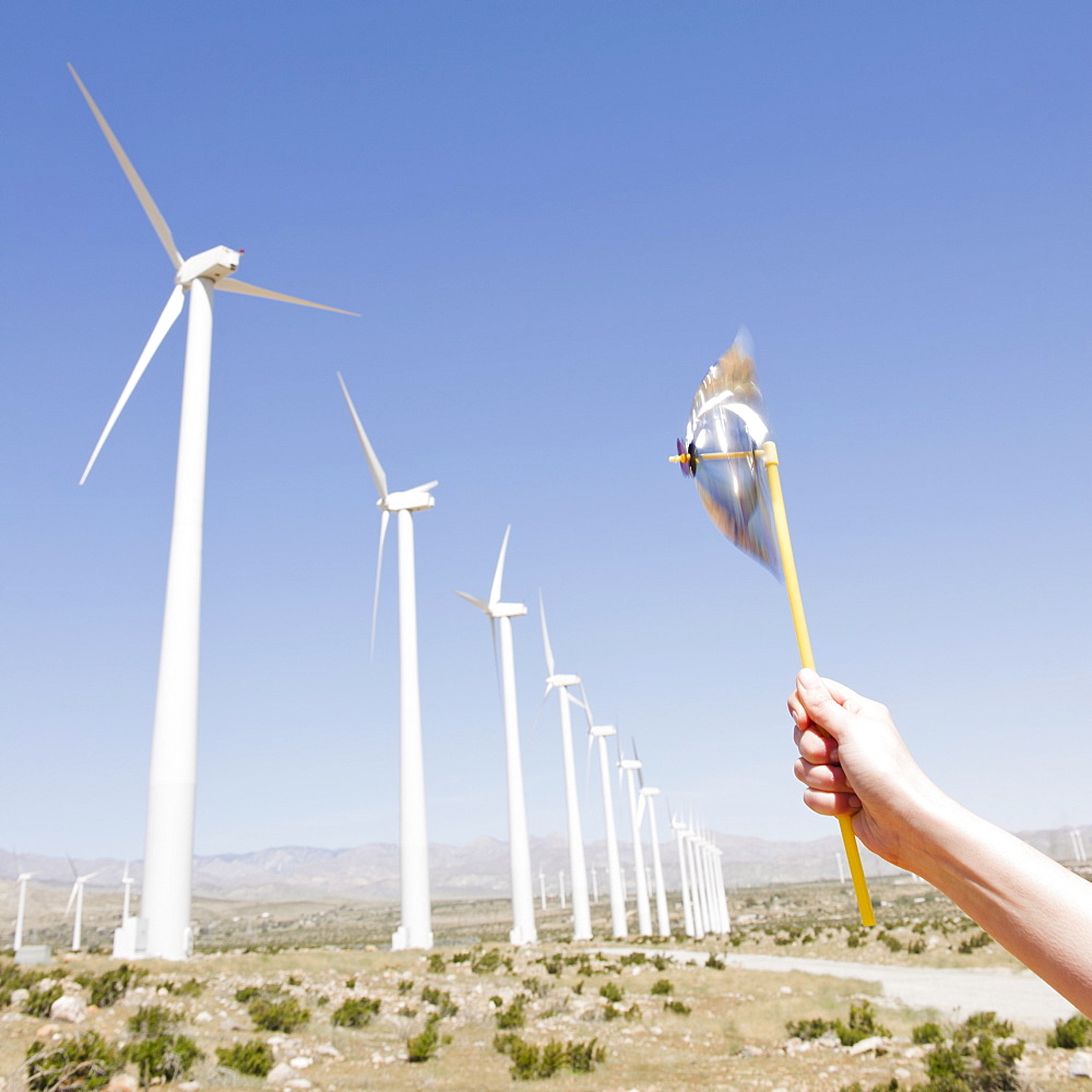 USA, California, Palm Springs, Coachella Valley, San Gorgonio Pass, Woman's hand holding pinwheel against blue sky and wind turbines