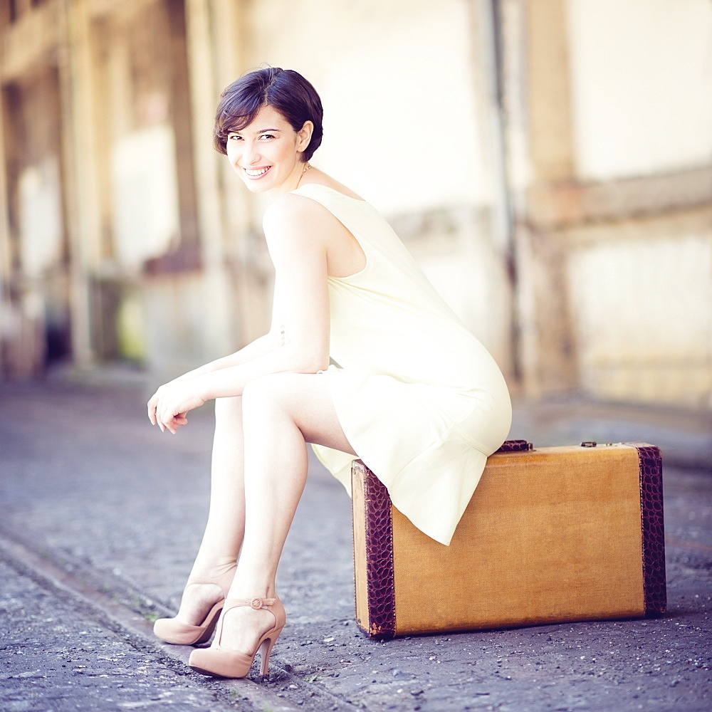 Woman in dress sitting on suitcase at train station, USA, New Jersey, Jersey City 