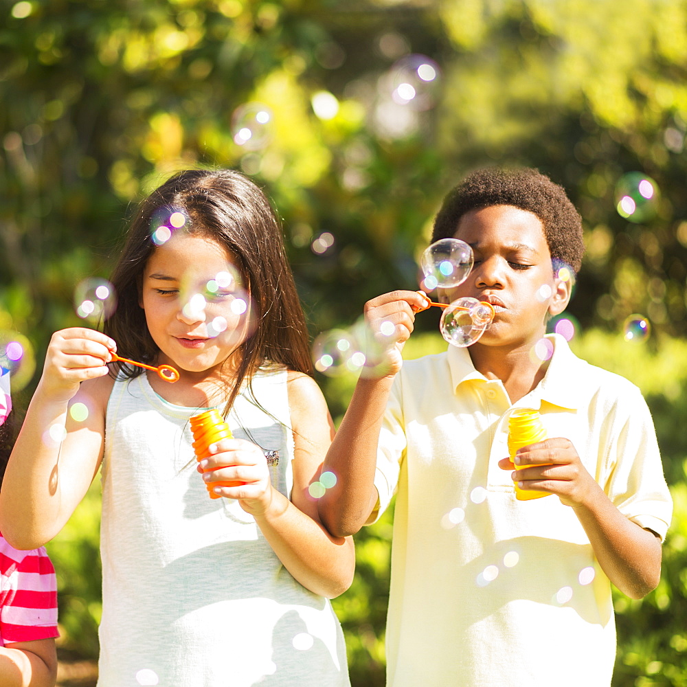 Girls( 4-5, 8-9) and boy (6-7) blowing soap bubble