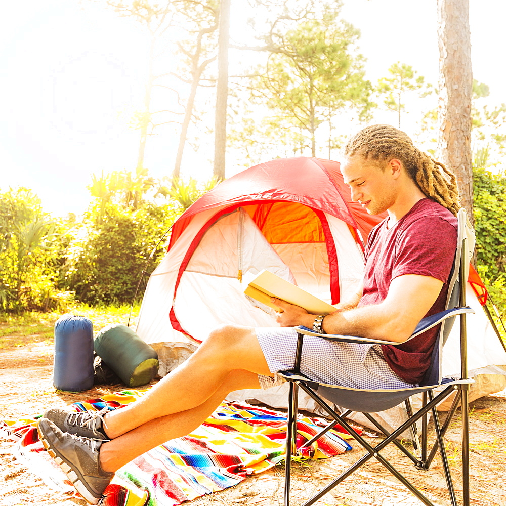 Man reading book in front of tent, Tequesta, Florida