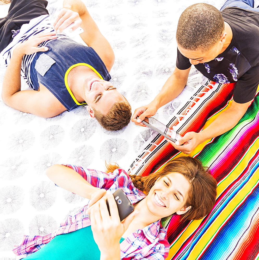 Young people lying on blanket, using technology