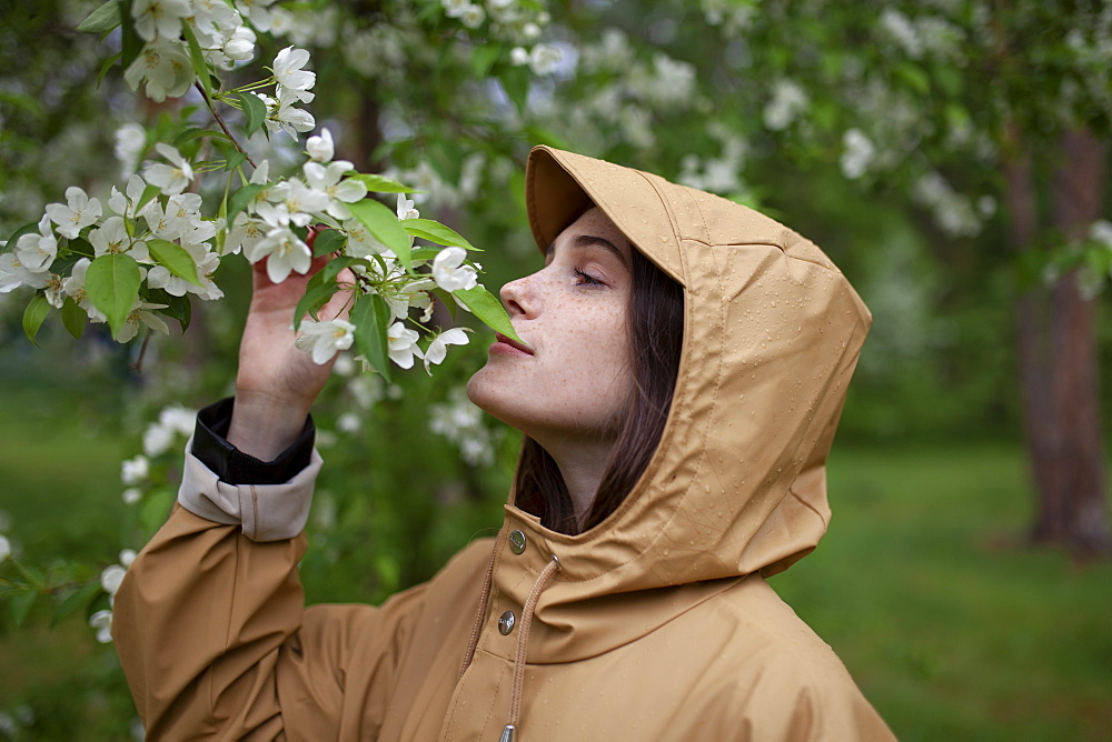 Young woman wearing brown raincoat sniffing flower