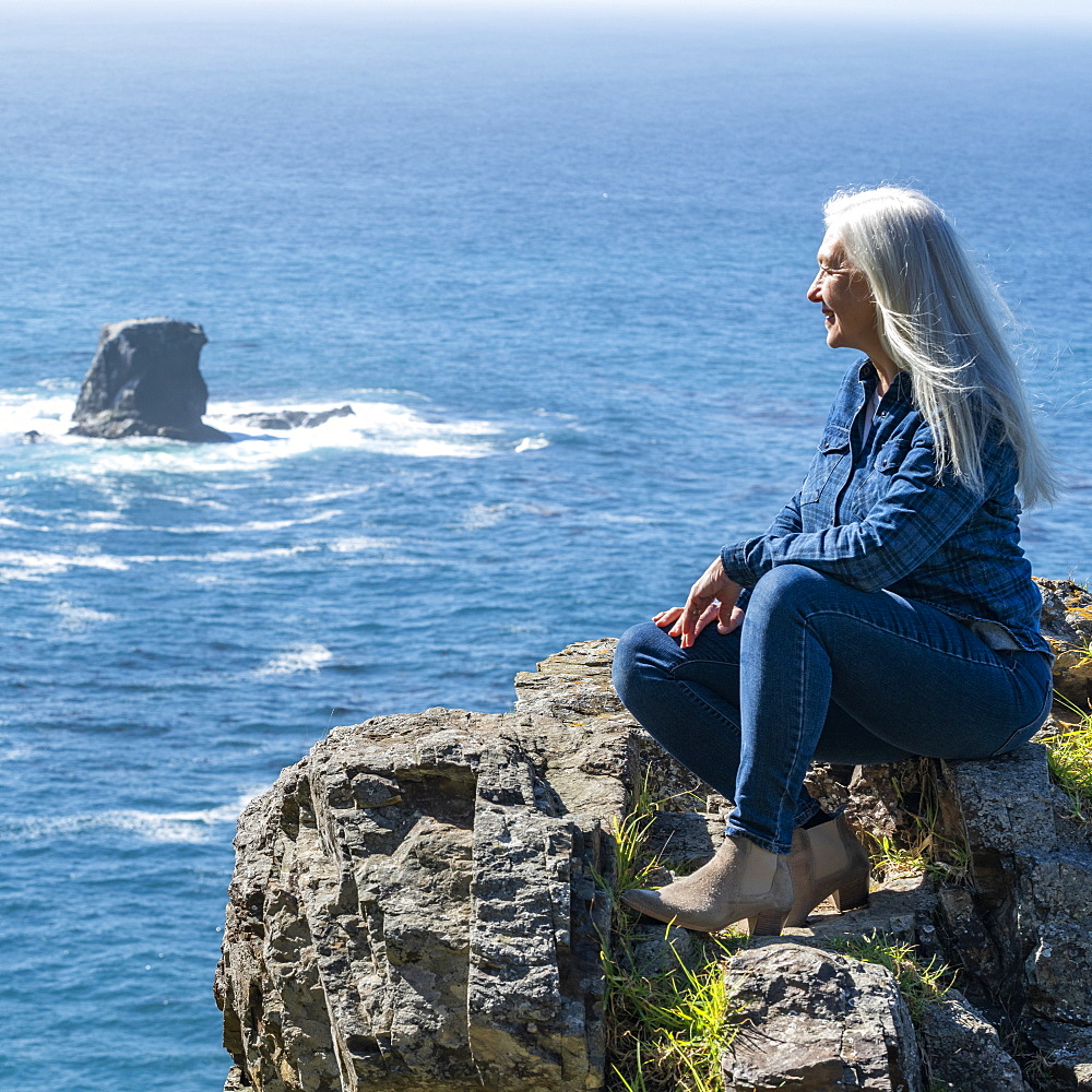 USA, California, Big Sur, Woman sitting at the edge of cliff looking at view