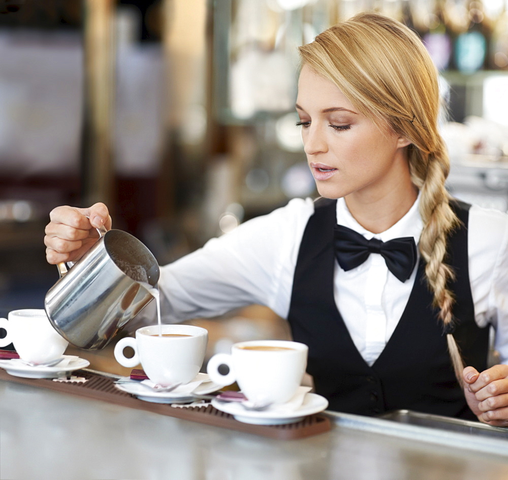 Female barista pouring milk into coffee cup