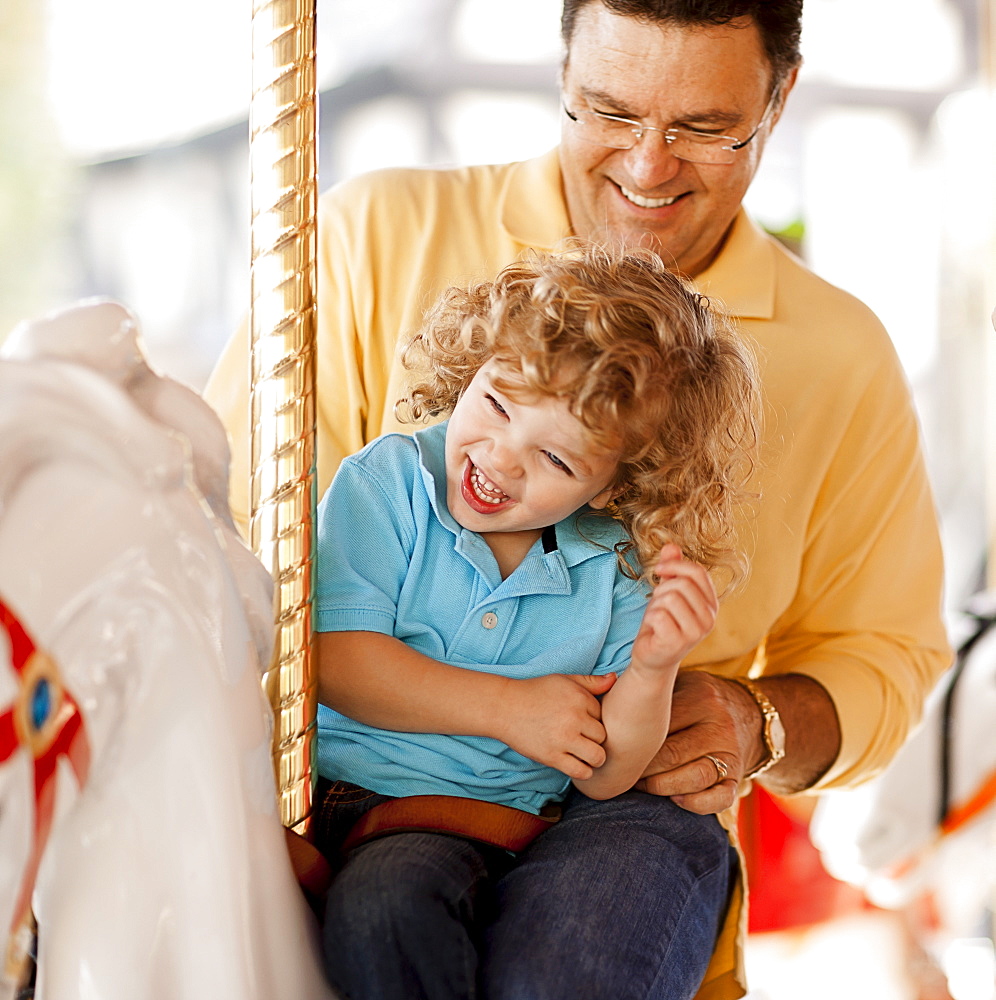 USA, California, Los Angeles, Father with son (4-5) sitting on carousel's horse