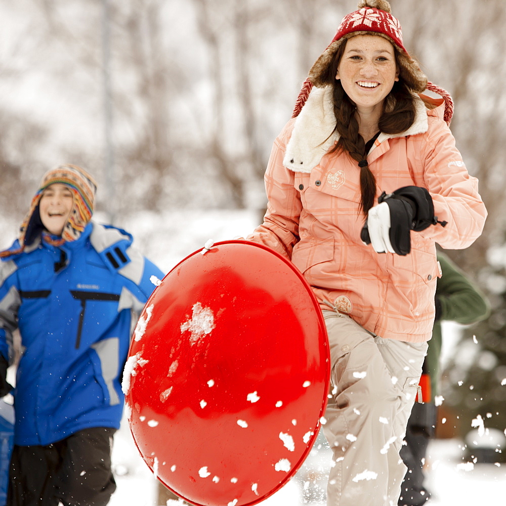 USA, Utah, Provo, Teenage (16-17) girl running with sledge, boys and girls (10-11, 12-13) in background