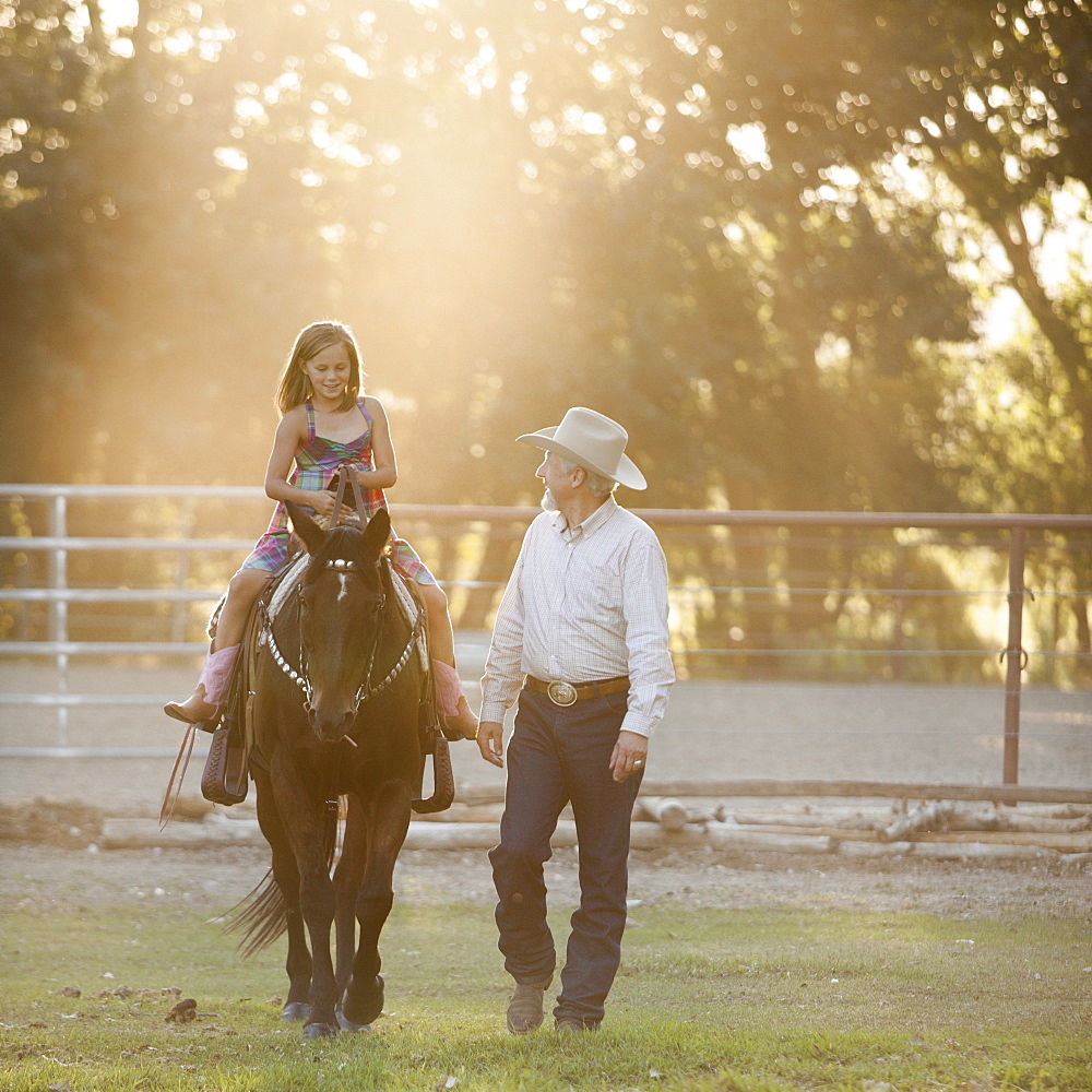 Trainer assisting girl (8-9) riding horse in paddock