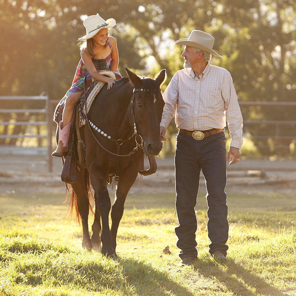 Senior man assisting granddaughter (8-9) horseback riding in ranch