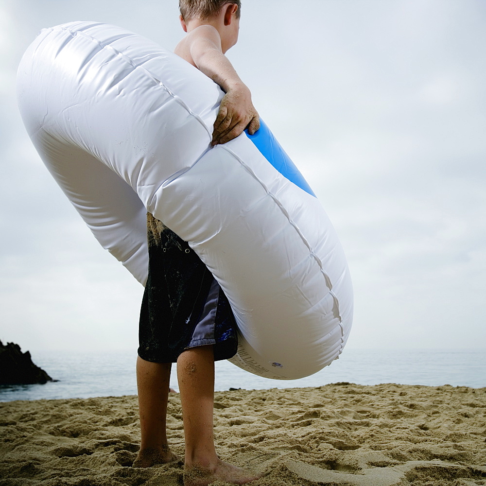 Young boy standing in an inflatable tube at the beach