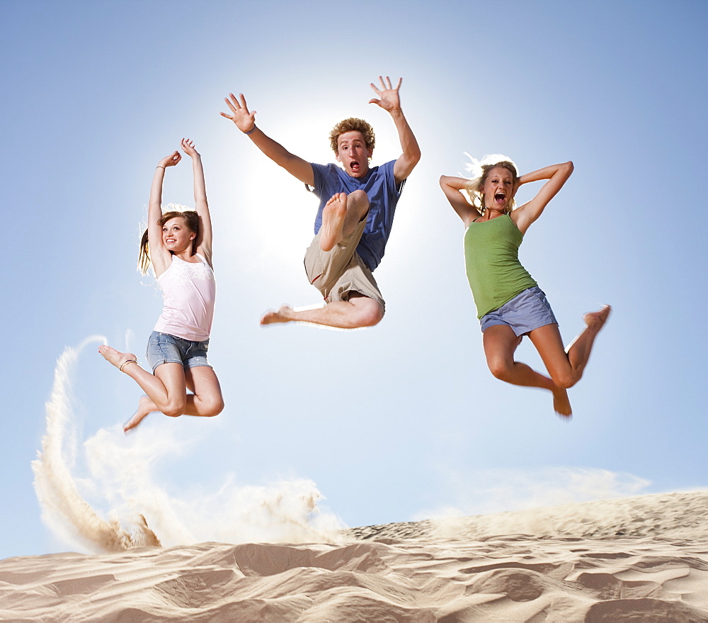 Three people jumping in the sand