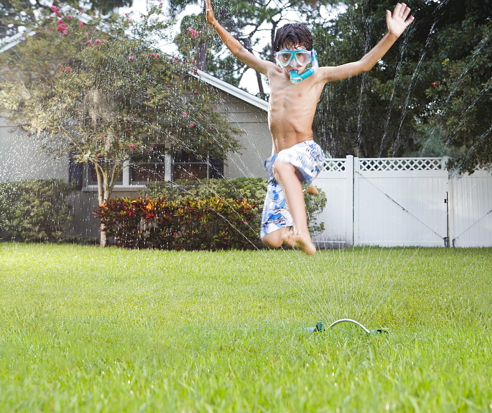 Boy jumping through sprinkler