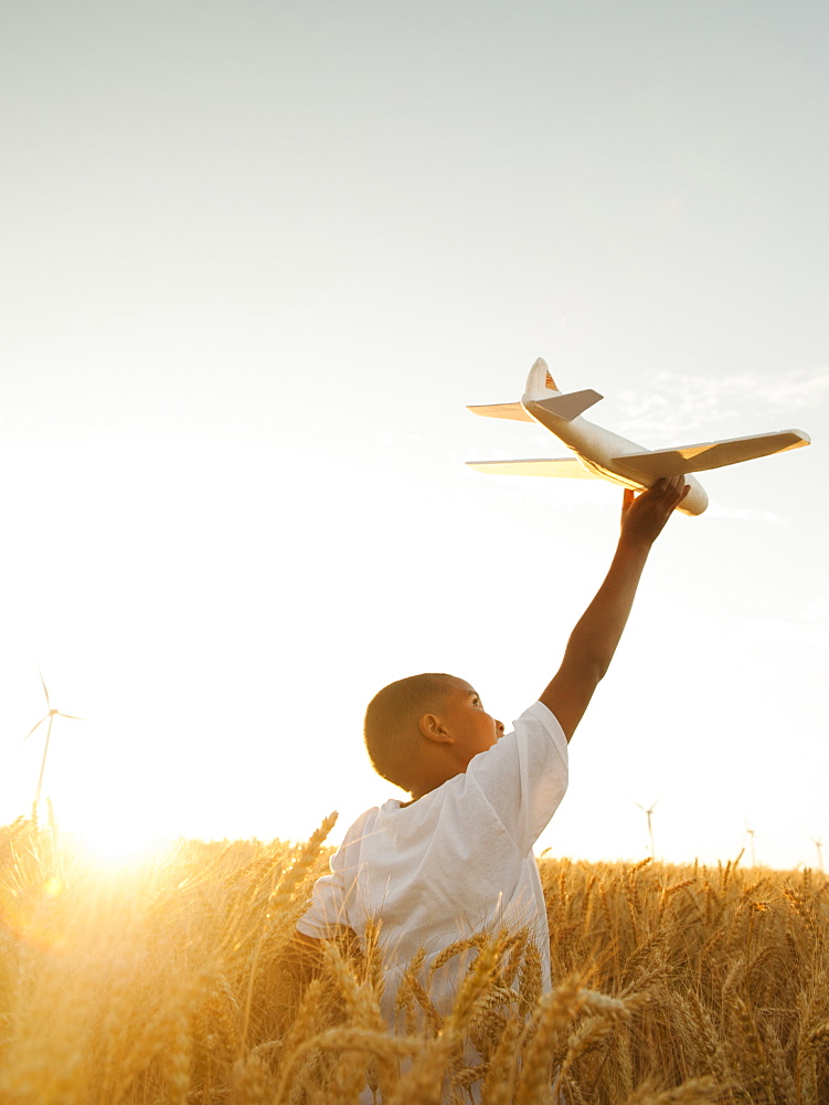 Boy (10-11) playing with toy aeroplane in wheat field