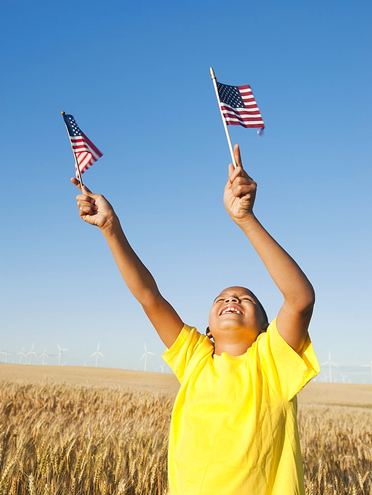 Boy (8-9) holding small american flags in wheat field