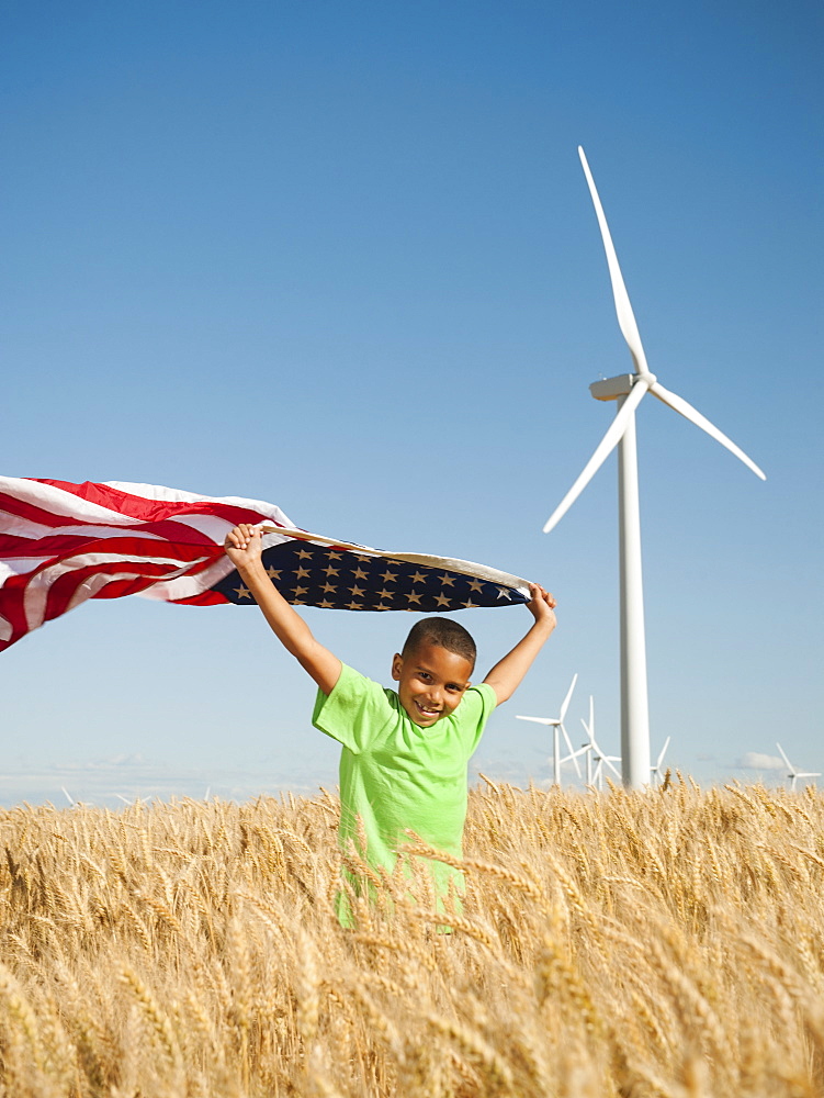 USA, Oregon, Wasco, Boy (8-9) flying american flag in wheat field with wind turbines in background