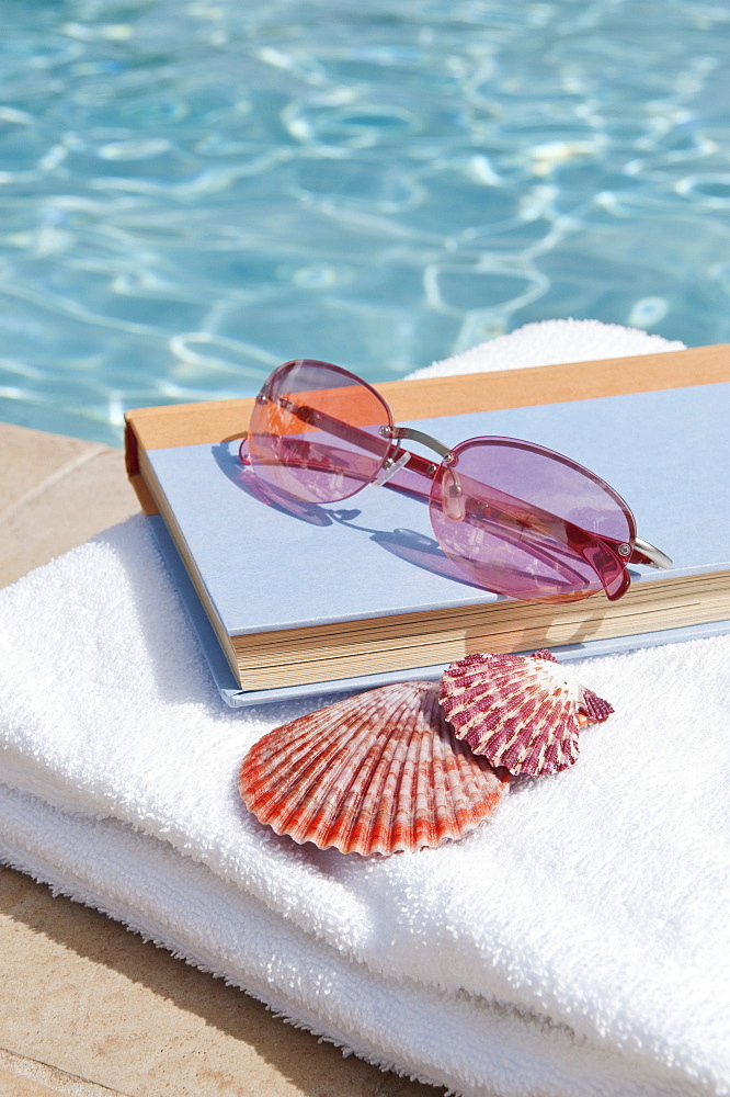 Book and sunglasses by swimming pool