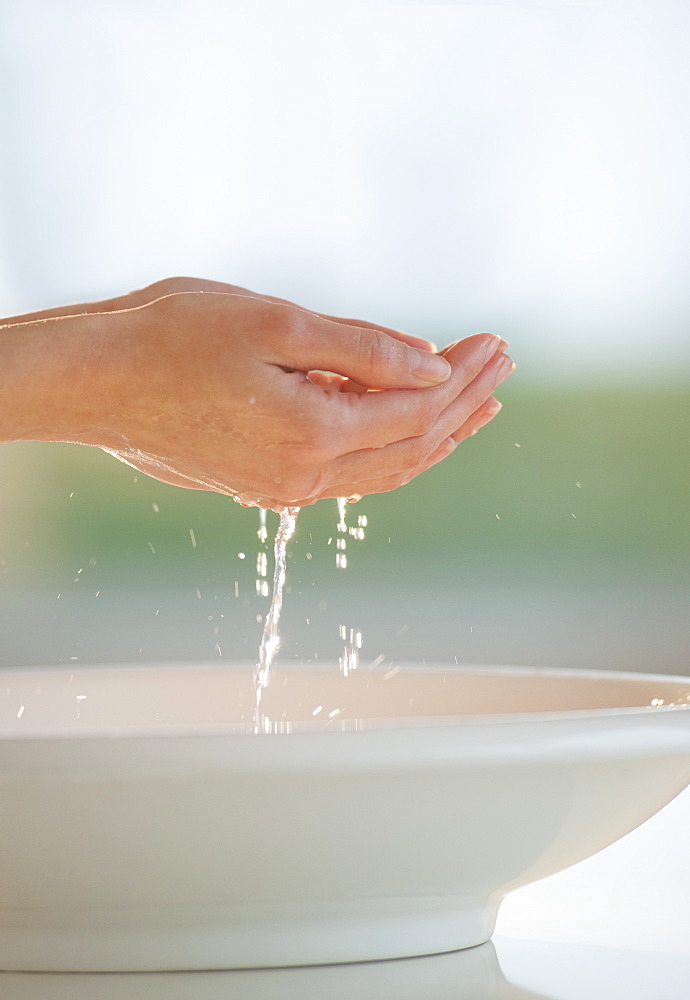 Water dripping from cupped hands over bowl